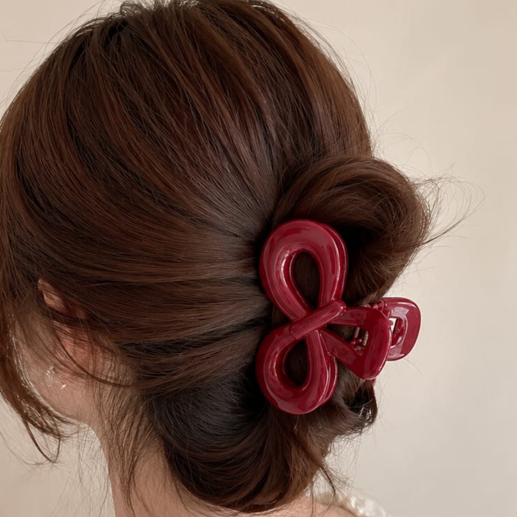 A glossy dark red hair claw clip holding a brown bun hairstyle, shown on a model from the back against a plain light beige background.