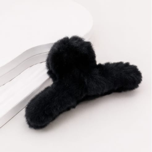 A black fluffy faux fur hair claw clip resting on a clean white surface.