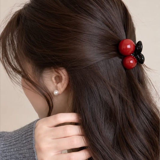 A close-up of a woman's hair secured with a decorative hair clip featuring two glossy red beads and one black bead, shown from the side.