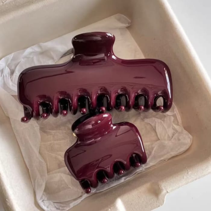 Two glossy deep burgundy hair claw clips resting on white tissue paper inside a beige tray.