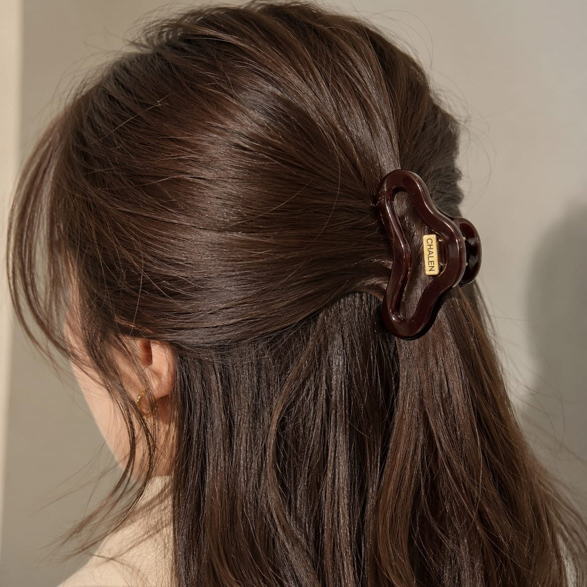 A close-up of a woman's brown hair secured with a dark brown claw clip, shown from the back against a soft neutral background.