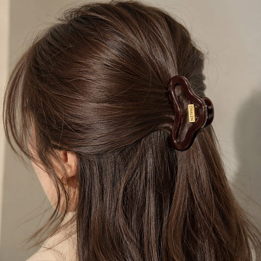 A close-up of a woman's brown hair secured with a dark brown claw clip, shown from the back against a soft neutral background.