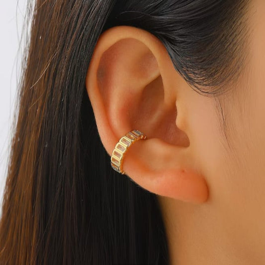 A close-up of a person's ear wearing a gold ear cuff with a textured segmented band and small clear stones.