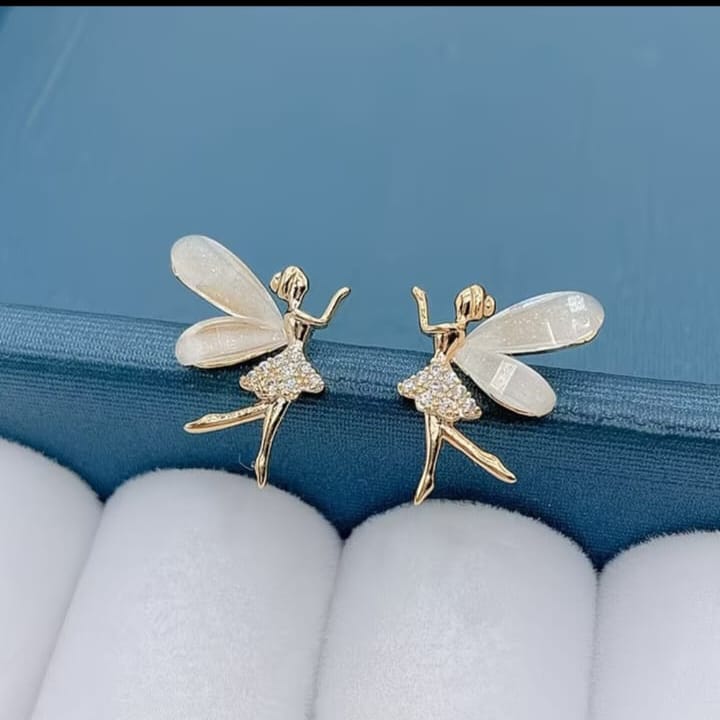 A pair of fairy-shaped stud earrings in gold-tone metal with iridescent white wings and a sparkling clear dress, displayed on a blue jewelry box cushion.