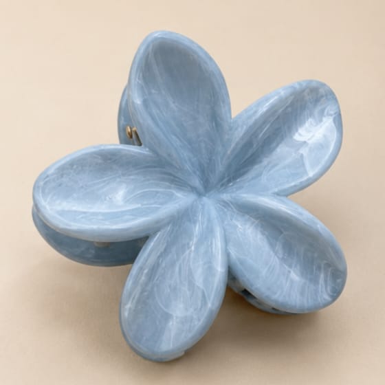 A light blue flower-shaped hair claw clip with a glossy, marbled texture, shown on a solid beige background.