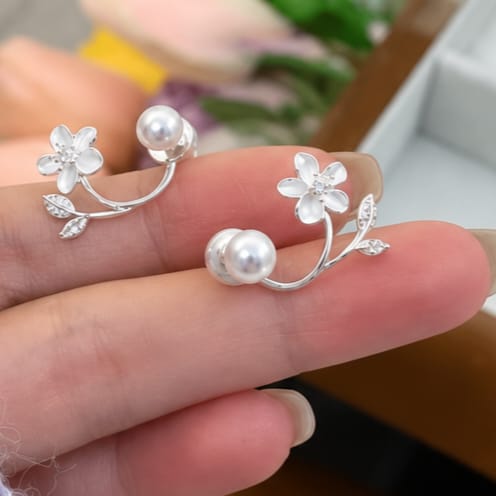 Silver floral ear cuffs with white pearl beads and small clear rhinestone accents, shown resting on a person's fingers.