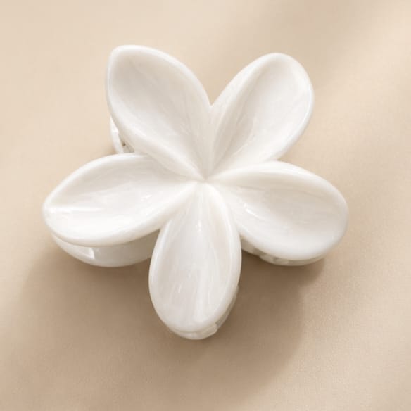 A white five-petal flower-shaped hair claw clip on a warm beige background.