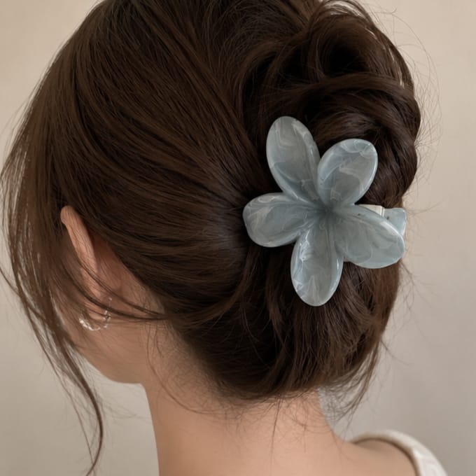 A light blue translucent flower-shaped hair claw clip holding a dark brown updo, shown on a model's head against a plain beige background.