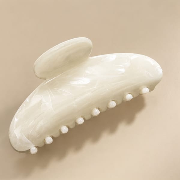 A glossy white hair claw clip with a small loop on the back, photographed on a plain beige background.