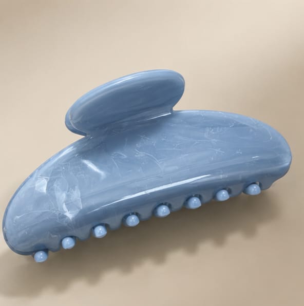 A light blue hair claw clip with a glossy finish and small raised teeth along the bottom, photographed on a plain beige background.