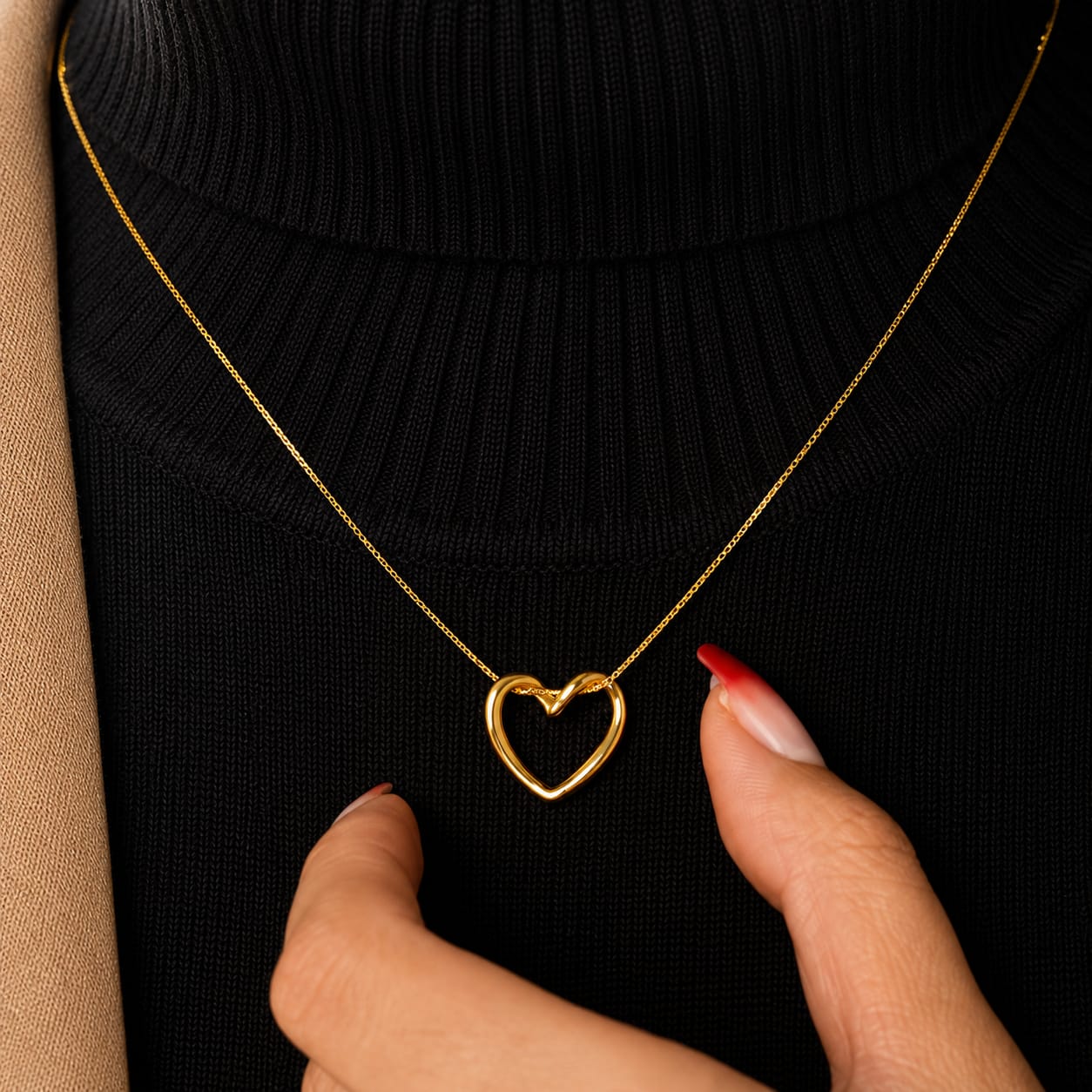 A gold heart-shaped open pendant necklace worn on a black ribbed turtleneck sweater, with a hand gently touching the pendant.