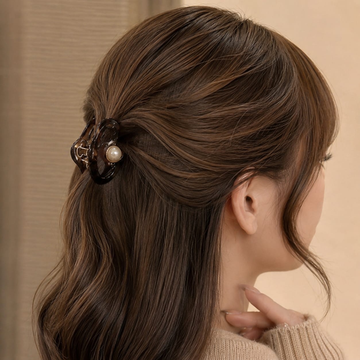 A woman shown from the back and side wearing a dark brown claw-style hair clip with a pearl accent, holding her half-up hairstyle.