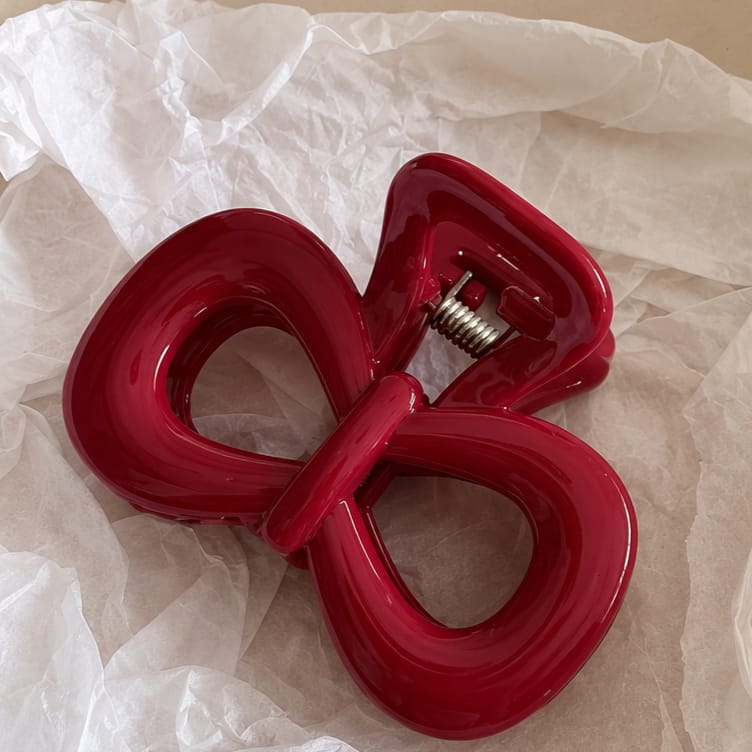 A glossy red bow-shaped hair claw clip resting on crumpled white tissue paper.
