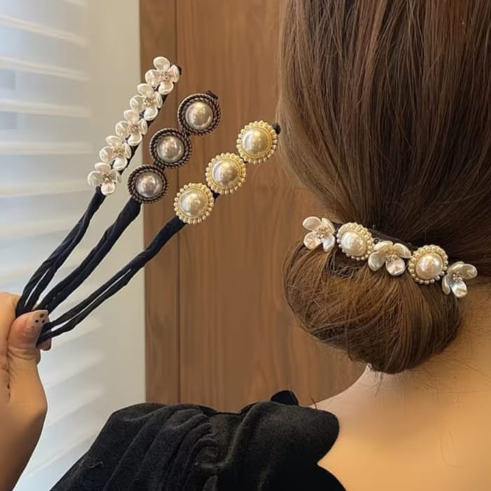 Three black hair accessory clips decorated with faux pearls and floral details, shown being held by a hand and worn in a woman's low bun.