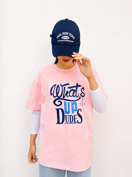 Model wearing pink graphic t-shirt with “Whats Up Dudes” print in a relaxed casual streetwear style by NUR