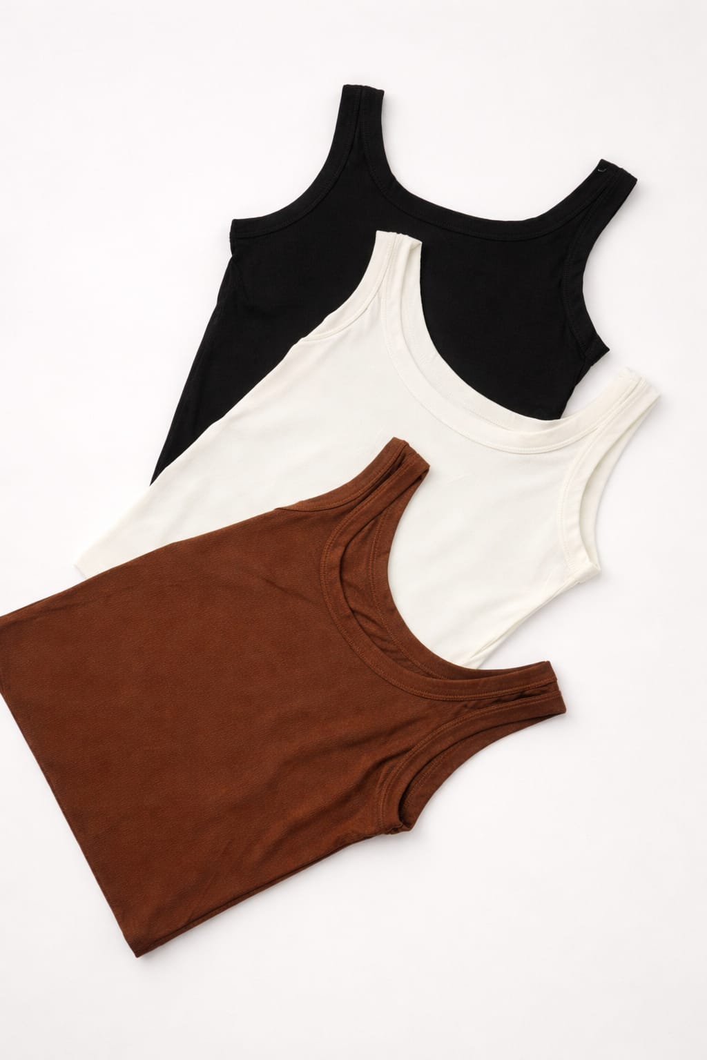 White, black, and brown ribbed tank tops by NUR displayed together, featuring fitted stretch design and modern everyday style